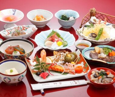 Assorted Japanese small plates with sashimi, tempura, pickles and lacquerware on red table