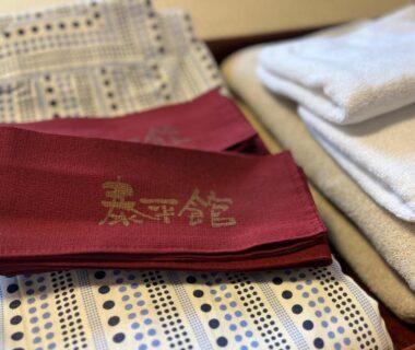 Folded patterned yukata with red sash embroidered Taiheikan and stacked towels at a ryokan in Yamanashi