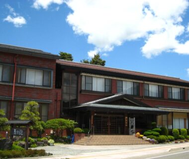 Three-story ryokan building with main entrance, manicured shrubs and clear blue sky in Yamanashi, Chūbu