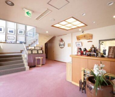 Carpeted ryokan lobby with wooden reception desk, stairs, framed art and orchid arrangement at Taiheikan, Yamanashi