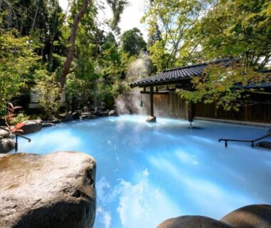 Milky-blue outdoor onsen surrounded by forest and traditional wooden ryokan architecture in Ōita