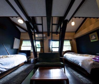 Twin room with exposed wooden beams, central low table and seating beneath windows at Taisho Yufu no Hana Ōita