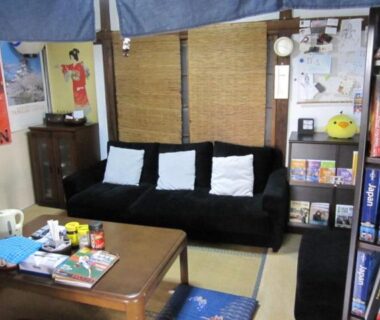 Tatami sitting area with low table, black sofa and bookshelf at Taito Ryokan in Tokyo