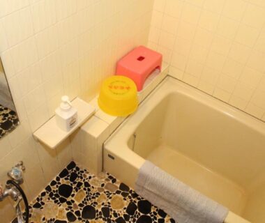 Compact bathroom with small soaking tub, plastic stool, basin, mirror and mosaic tiled floor at Takahan Niigata