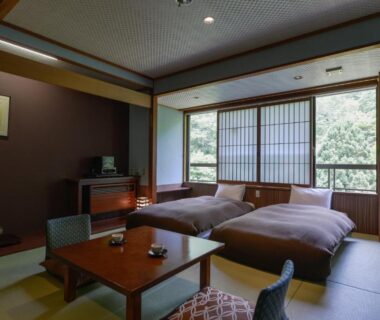 Low table, tatami flooring, twin futon beds, shoji window with trees outside at Takamiya Bettei Kuon Yamagata