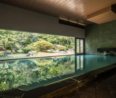 Spacious indoor onsen with large window framing manicured garden at Takamiya Bettei Kuon, Yamagata