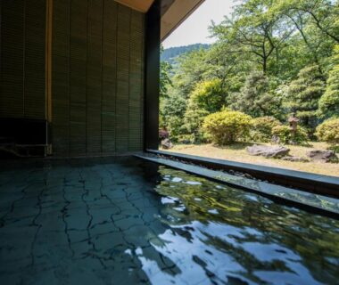 Interior onsen bath overlooking landscaped garden and forest at Takamiya Bettei Kuon in Yamagata