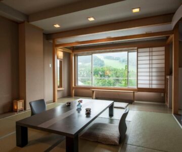 Traditional tatami room with low table, floor chairs, shoji window and green mountain view in Yamagata