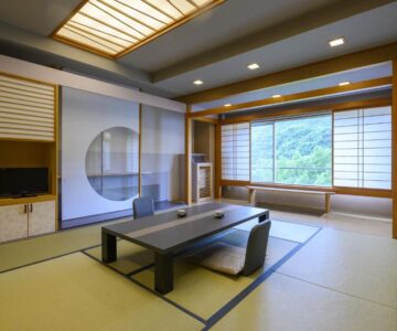 Traditional tatami room with low table, shoji screens, and window overlooking green hillside at Takamiya Hotel Lucent, Yamagata