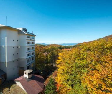 Hotel exterior beside vibrant autumn trees and distant mountains in Yamagata, Tōhoku, Japan
