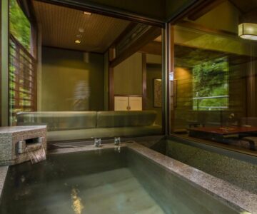 Stone indoor onsen with wooden interior and view into tatami room at Takamiya Ryokan Miyamaso Yamagata