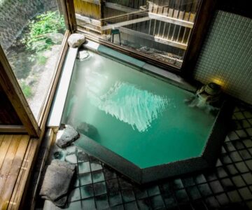 Indoor tiled onsen bath with wooden deck and garden view at Takamiya Ryokan Miyamaso, Yamagata, Tōhoku, Japan