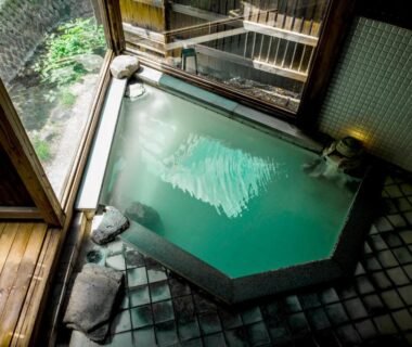Indoor tiled onsen bath with wooden deck and garden view at Takamiya Ryokan Miyamaso, Yamagata, Tōhoku, Japan