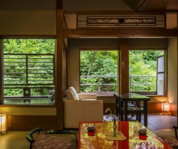 Traditional tatami room with low table, sofa seating and lush greenery outside at Takamiya Ryokan Miyamaso, Yamagata