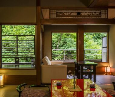 Traditional tatami room with low table, sofa seating and lush greenery outside at Takamiya Ryokan Miyamaso, Yamagata