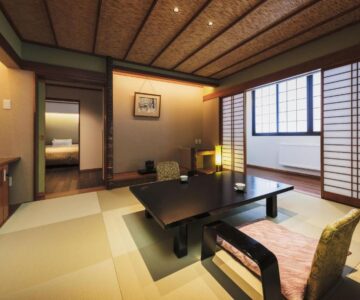 Tatami room with low table, shoji screens and a bedroom visible through the doorway at Takamiya Ryokan Miyamaso, Yamagata