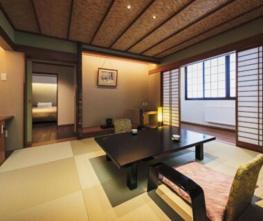 Tatami room with low table, shoji screens and a bedroom visible through the doorway at Takamiya Ryokan Miyamaso, Yamagata