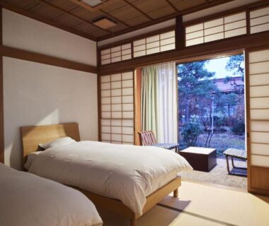 Tatami-floored twin bedroom with shoji screens and sliding doors opening to a small garden at Takamiya Ryokan, Yamagata