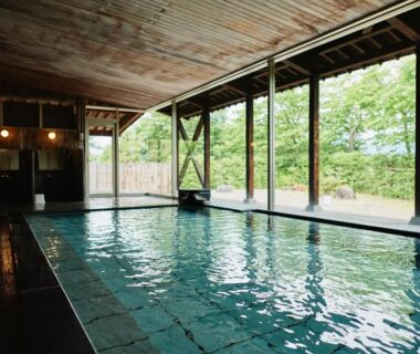 Tiled indoor onsen with wooden ceiling and large windows overlooking garden at Takamiya Ryokan Sagiya Sansorai Yamagata
