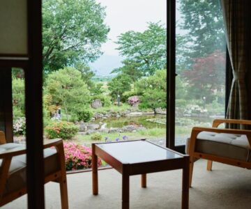 Tatami room with low table and chairs opening onto landscaped garden and pond at Takamiya Ryokan Sagiya Sansorai Yamagata