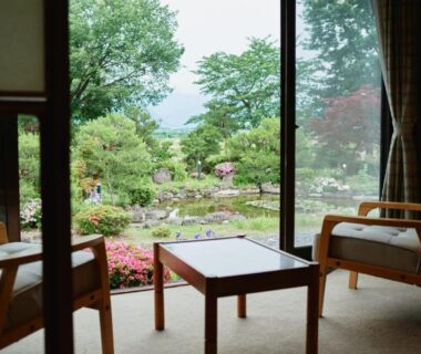 Tatami room with low table and chairs opening onto landscaped garden and pond at Takamiya Ryokan Sagiya Sansorai Yamagata