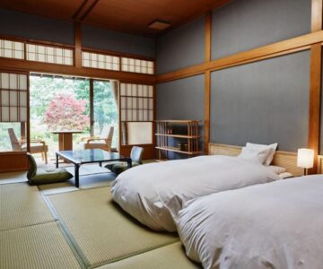 Tatami room with low beds, shoji screens and table, sliding doors to garden at Takamiya Ryokan Sagiya Sansorai Yamagata