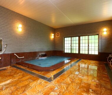 Rectangular indoor onsen with tiled marble floor, wooden walls, wall-mounted showers and large sliding windows at Takanoya, Niigata