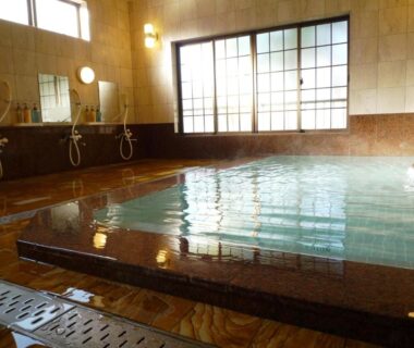 Indoor communal onsen bath with tiled edge, wall-mounted showers and shoji-style windows at Takanoya in Niigata