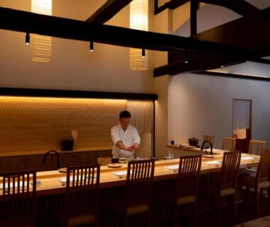 Chef preparing food behind wooden dining counter with bar seating and warm pendant lighting at Takanoya, Niigata