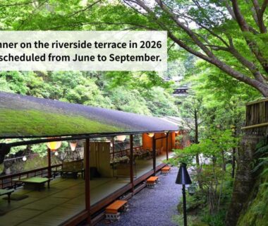 Covered riverside wooden terrace with seating beside lush trees and a stone path at Takao Kanko Hotel, Kyoto