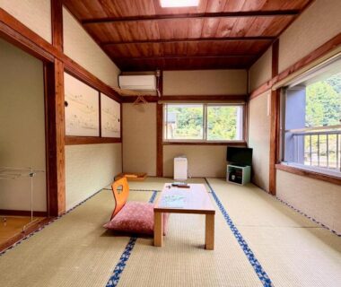 Tatami room with low table, floor cushions, wooden ceiling and windows overlooking greenery at Takaosou Ōita