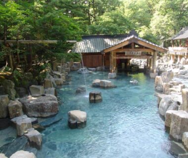 Outdoor rock-lined onsen pool with wooden bathhouse at Takaragawa Onsen Ousenkaku in Gunma, Japan