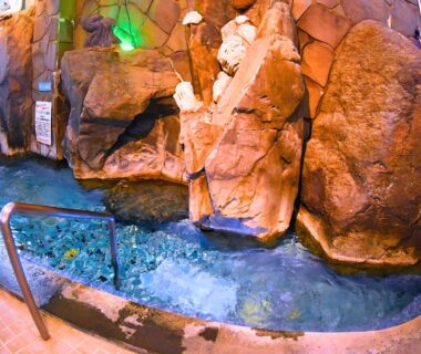 Indoor blue onsen bath with rocky walls and handrail at Takasago Onsen in Hokkaidō