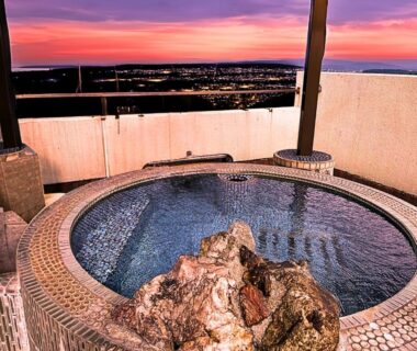 Circular rooftop onsen bath with tiled edge and city sunset view at Takasago Onsen, Hokkaidō