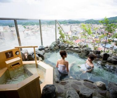 Guests relaxing in a rooftop stone onsen with city and mountain views at Takayama Ouan, Gifu