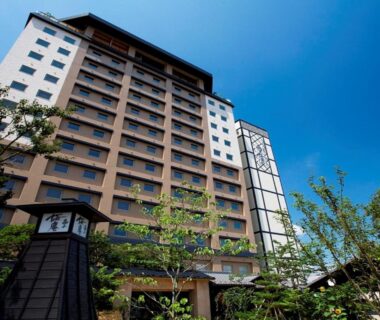Multi-story ryokan exterior with clear blue sky and trees at Takayama Ouan in Gifu