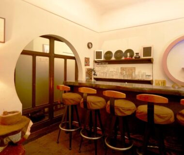 Interior bar counter with wooden stools, round window and warm lighting at Takeyaso Ryokan in Hyōgo