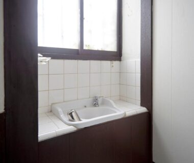 Compact tiled basin with faucet beneath wooden window at Takeyaso Ryokan, Hyōgo
