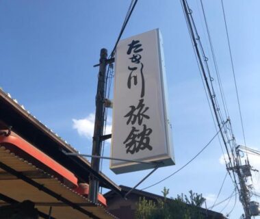 Vertical sign with kanji characters for Takigawa Ryokan, street and utility poles under clear blue sky in Kyoto