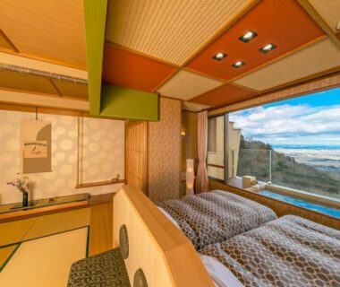 Twin beds and tatami seating beside large window with coastal view at Takimotokan Yuki No Sato Gifu