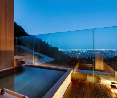 Outdoor wooden bath with glass railing overlooking city lights and mountains at Takimotokan Yuki No Sato, Gifu, Chūbu Japan