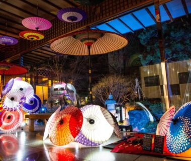 Illuminated traditional wagasa umbrellas arranged indoors at Takuboku Tei, Hokkaidō, reflecting on wet floor