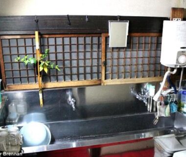 Compact stainless sink and kitchenette with water heater, storage shelves, and shoji-style window at Tama Ryokan Tokyo
