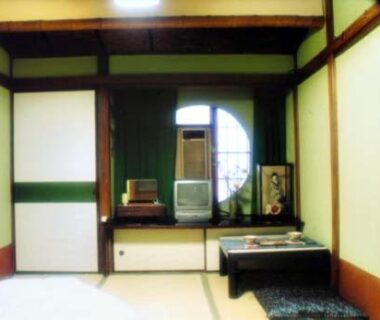Traditional tatami room with low table, shoji screens and circular window at Tama Ryokan in Tokyo