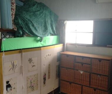 Small storage area with stacked woven baskets, low television, curtains and a compact kitchenette at Tama Ryokan, Tokyo