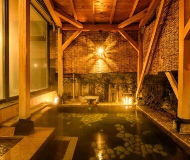 Warm-lit covered onsen with wooden beams, stone edging and bamboo screens at Tamaya Ryokan Nagano