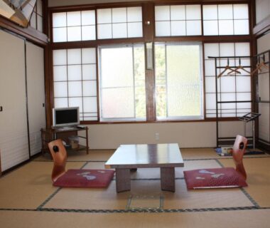 Traditional tatami room with low table, zabuton cushions, shoji screens, small TV and wall hanger rack in Tamonkan Yamagata