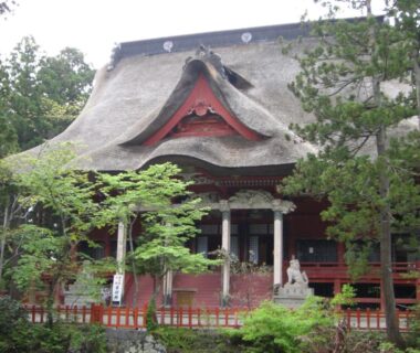 Thatched roof red temple-like building at Tamonkan in Yamagata, surrounded by trees