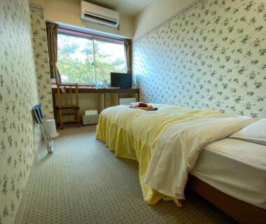 Twin beds, floral wallpaper, small desk and window showing greenery at Tango Onsen Hashiudosou Kyoto