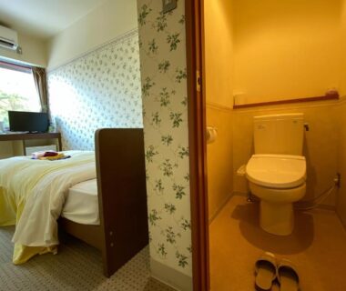 Twin beds, bedside table, window, TV, and separate toilet cubicle with slippers at the ryokan in Kyoto